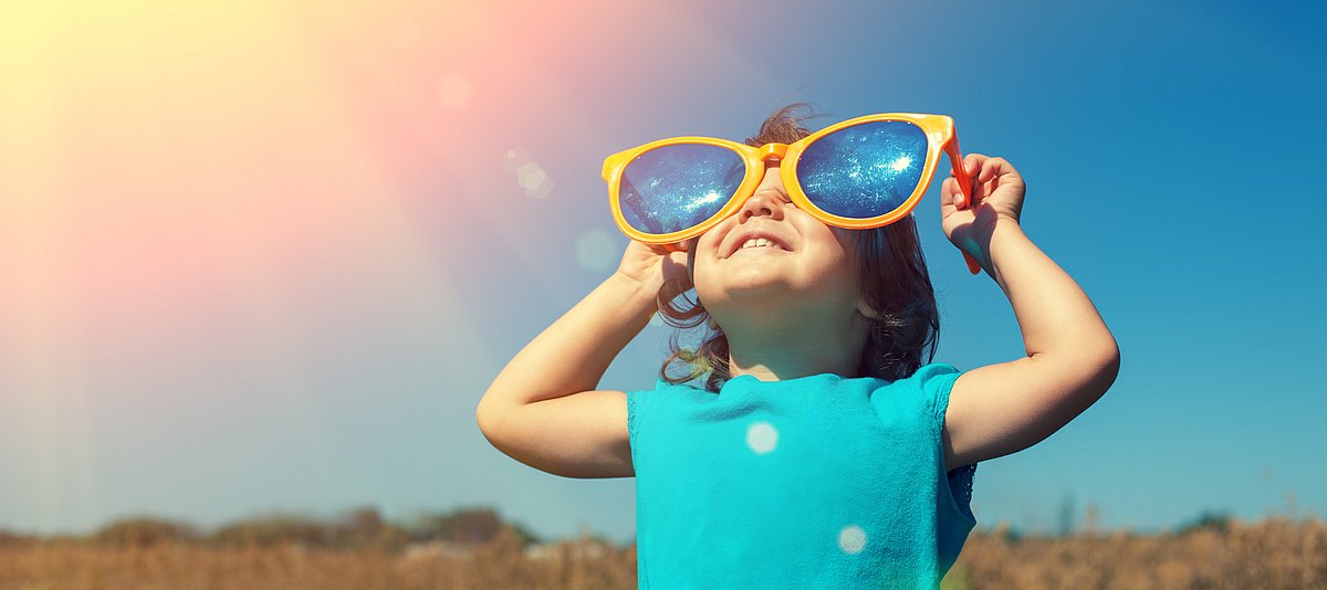 Kind mit großer Sonnenbrille guckt in den Himmel