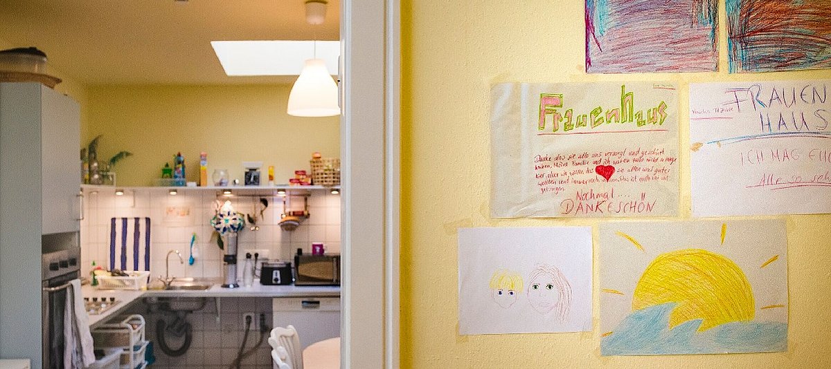 Küche und Gemeinschaftsbereich in einem Frauenhaus. Es hängen bunte Bilder an der Wand.