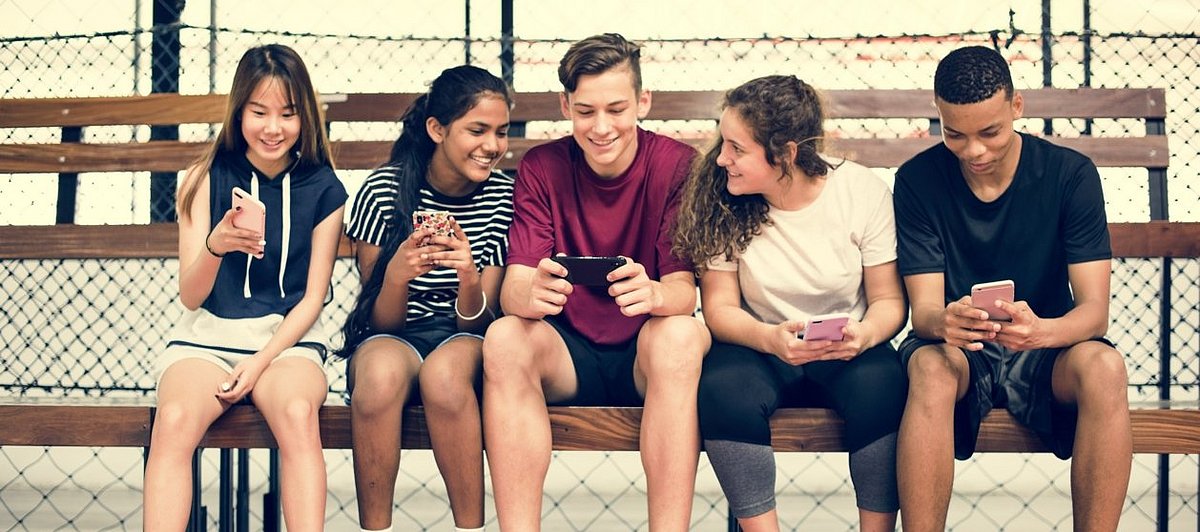 Eine Gruppe Jugendlicher sitzt auf einer Bank und die meisten haben ihre Smartphone in den Händen