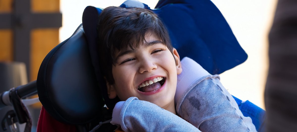Kind mit Beeinträchtigung im Rollstuhl lacht in die Kamera