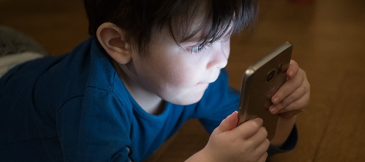 Ein kleiner Junge schaut gebannt auf das leuchtende Display eines Smartphones