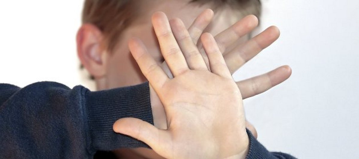 Junge hält Hände schützend vors Gesicht