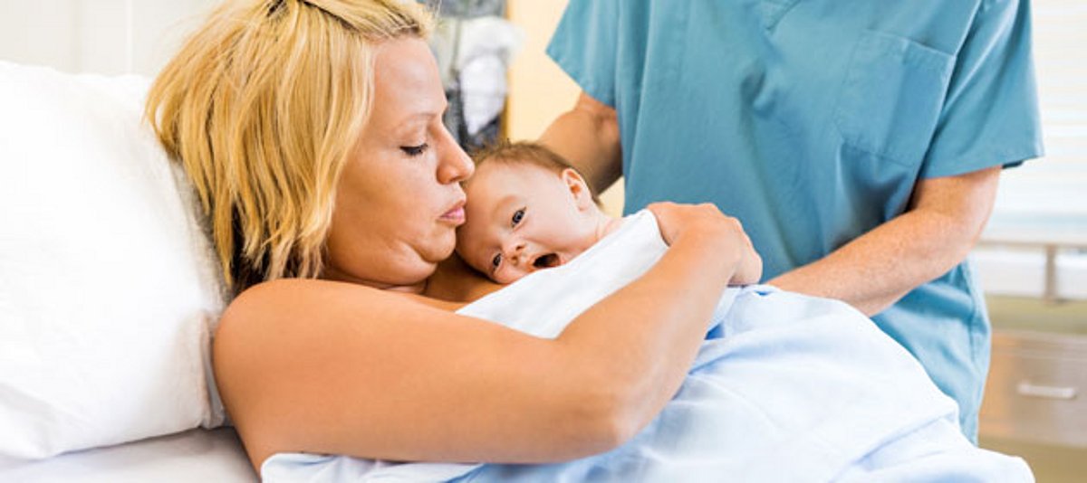 Mutter im Krankenhausbett hält Neugeborenes in den Armen