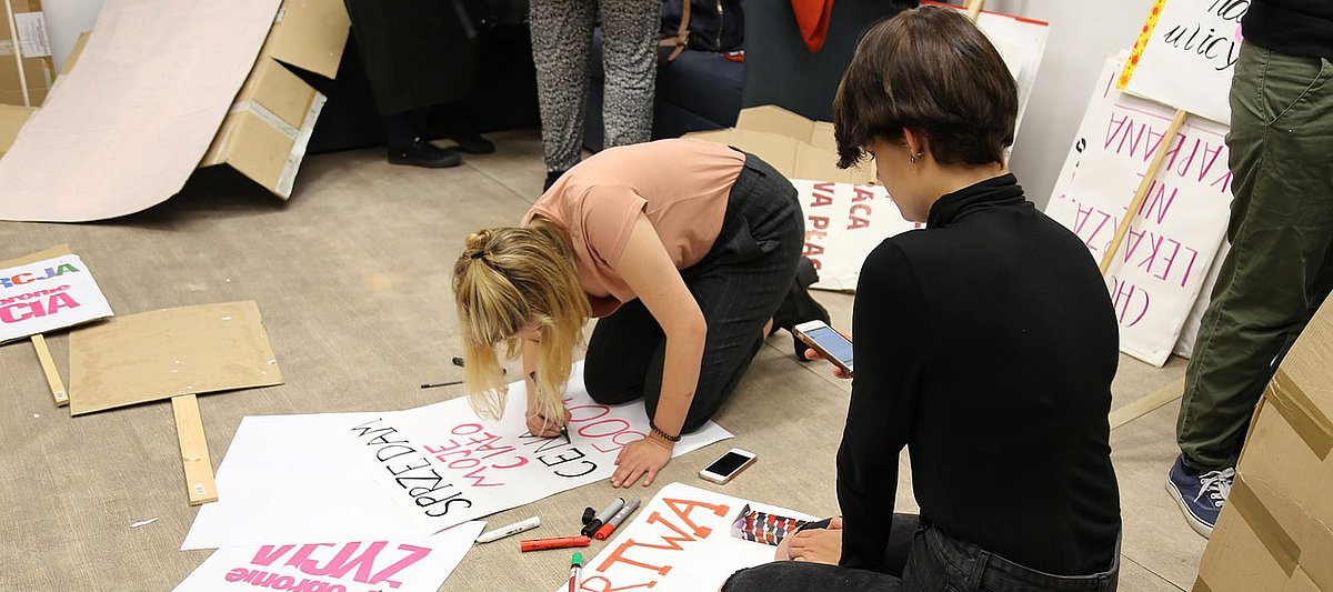 Jugendliche sitzen auf dem Boden und gestalten Plakate mit Slogans.