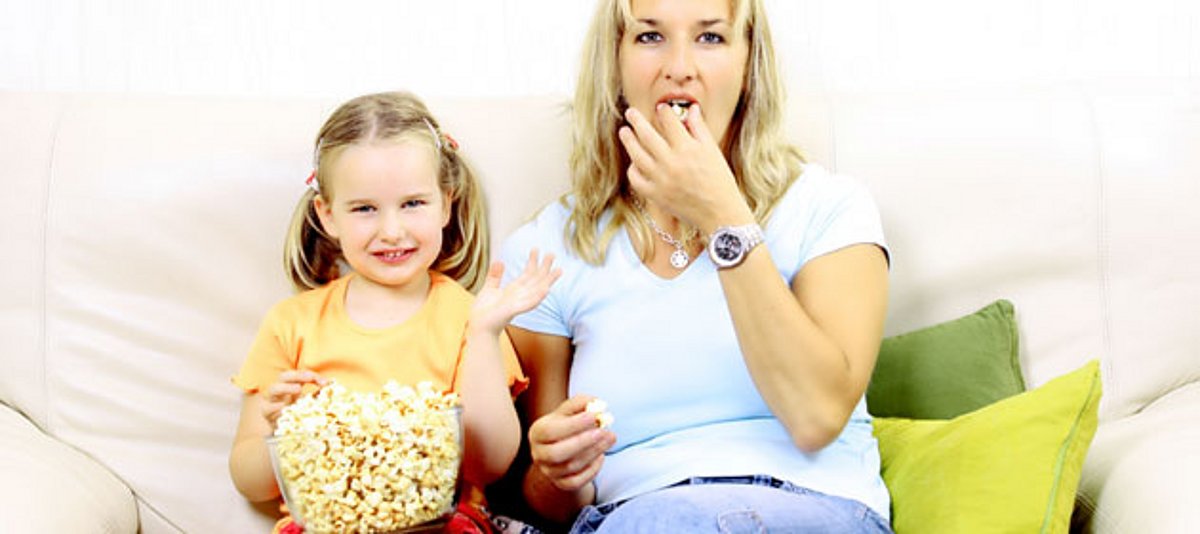 Mutter und Tochter schauen fern und essen Popcorn
