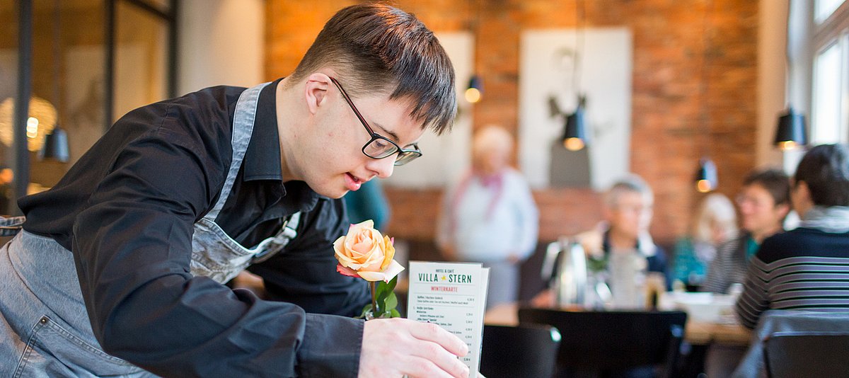 Ein junger Mann mit Down-Syndrom deckt einen Tisch in einem Restaurant