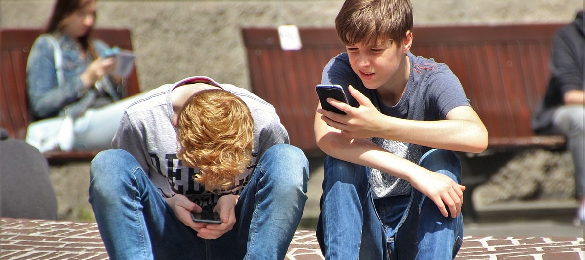 Zwei Jungen sitzen in einer Fußgängerzone und schauen ansgestrengt auf ihre Handys