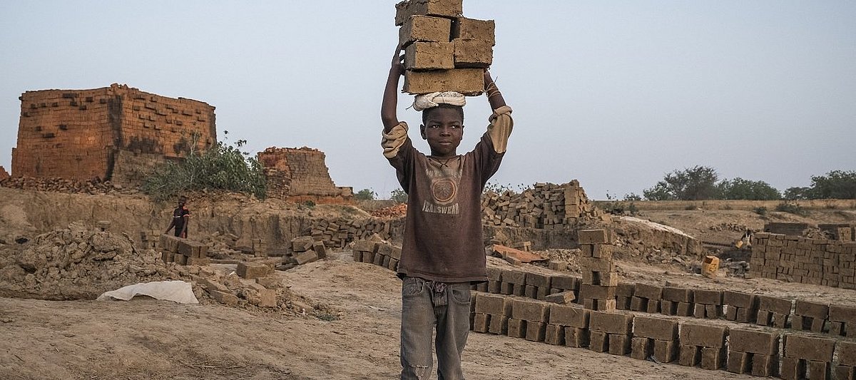Ein afrikanisches Kind transportiert schwere, große Steine auf dem Kopf.