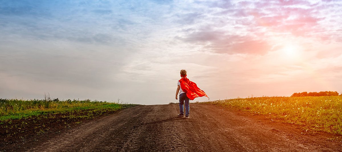 Ein Junge mit Superheld-Umgang läuft auf einem Feldweg entlang.