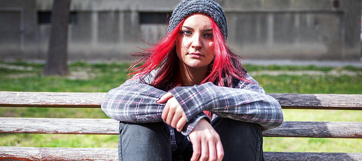 Eine junge Erwachsene mit roten Haaren und Mütze sitzt auf einer Wiese