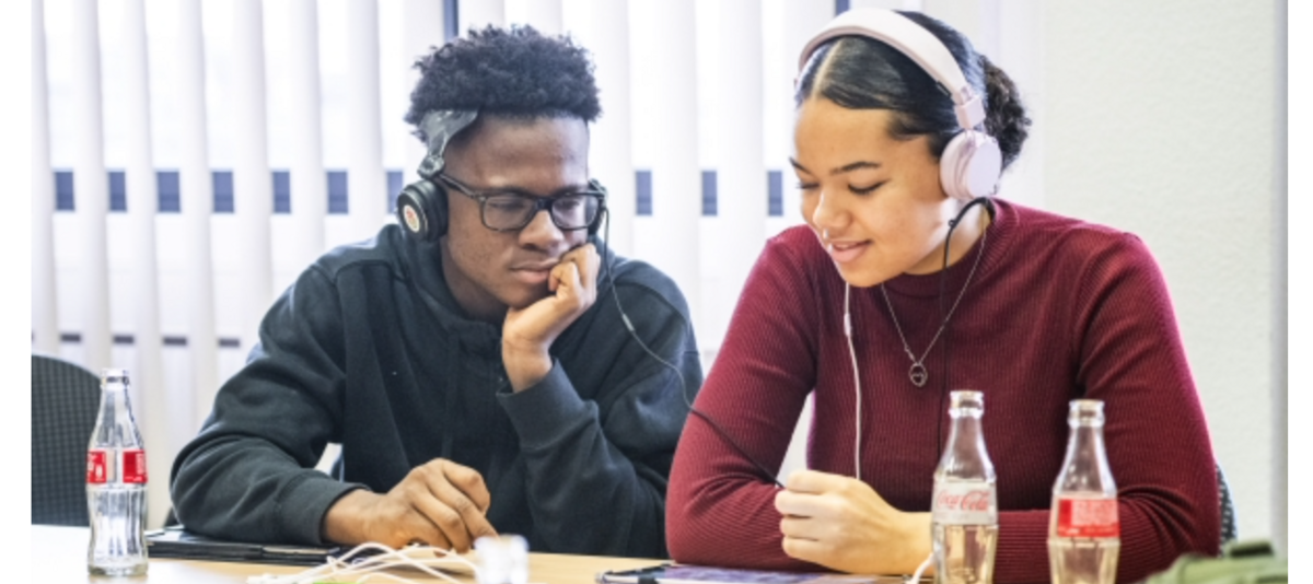 Zwei junge Menschen arbeiten an einem Musikprojekt, sie tragen Kopfhörer und schauen auf ein Tablet