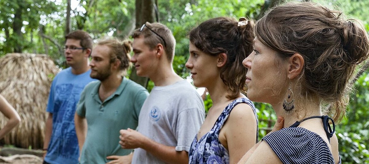 Fünf junge Menschen stehen im Wald und hören zu