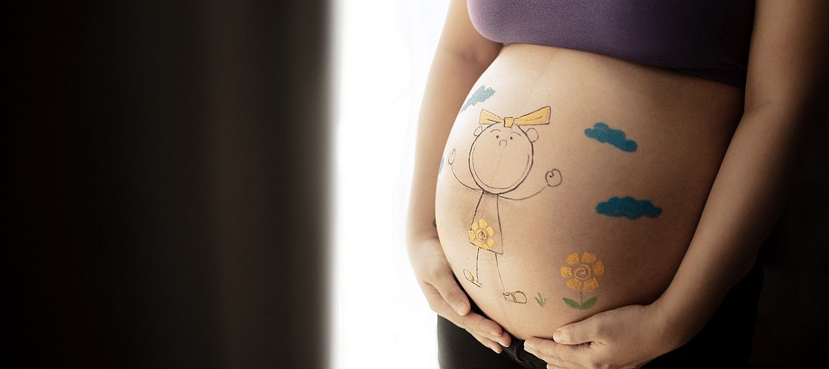 Eine schwangere Person hält mit den Händen ihren Bauch, der bunt bemalt ist