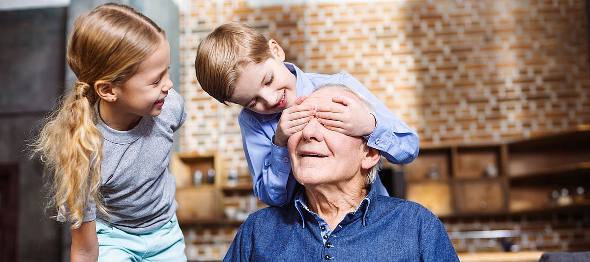 Ein Großvater spielt mit seinen Enkelkindern und der kleine Junge hält ihm die Augen zu.