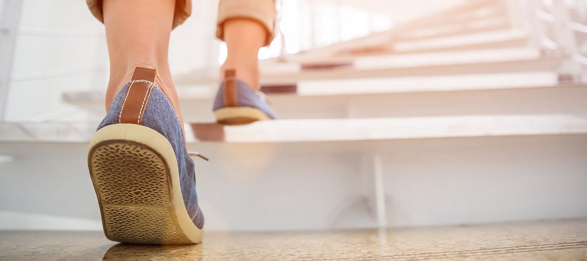 Eine junge Frau geht eine Treppe in einem Gebäude hoch, wobei nur ihre Füße zu sehen sind.