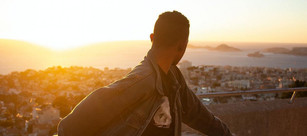 Ein junger Mann blickt über die Schule zurück über Marseille auf die untergehende Sonne.