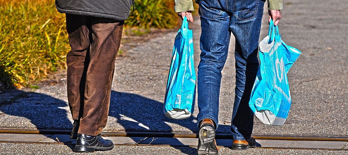 Ein junger Mann mit Einkaufstüten und ein älterer Männer laufen auf dem Gehweg