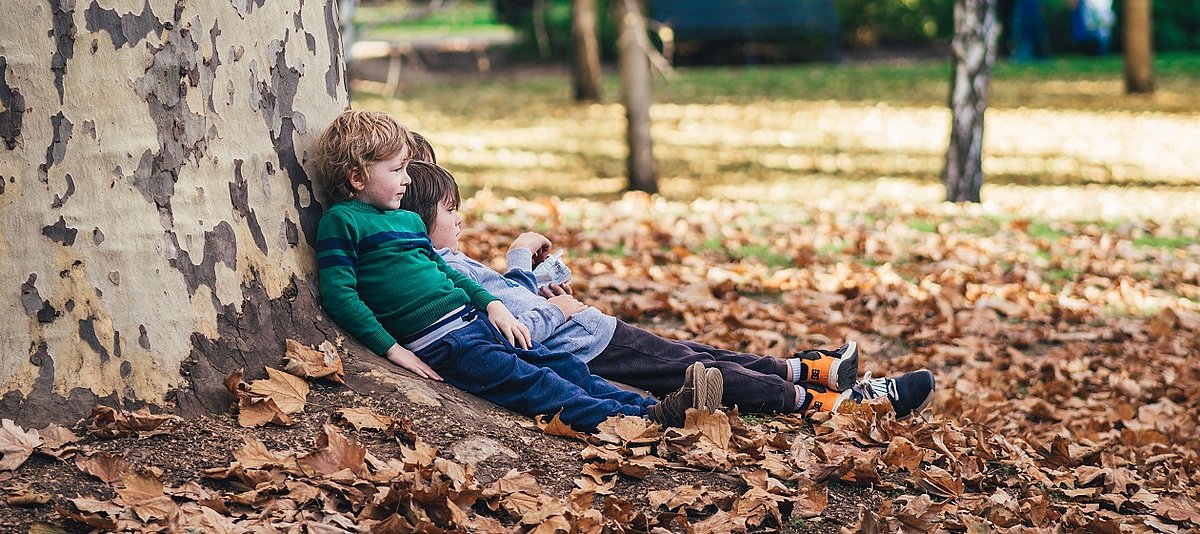 Drei Kinder sitzen unter einem Baum im Herbst