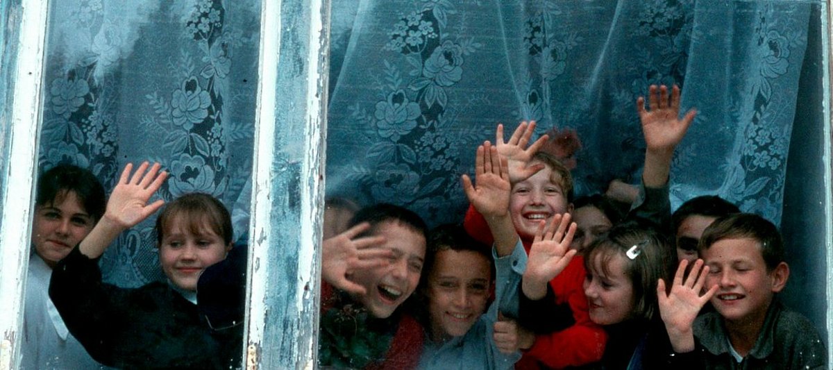Lachende Kinder stehen hinter einem Fenster und winken.