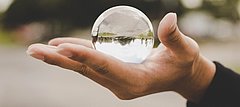 In einer Glaskugel, die jemande in der geöffneten Hand hält, spiegelt sich verkehrt herum eine Landschaft