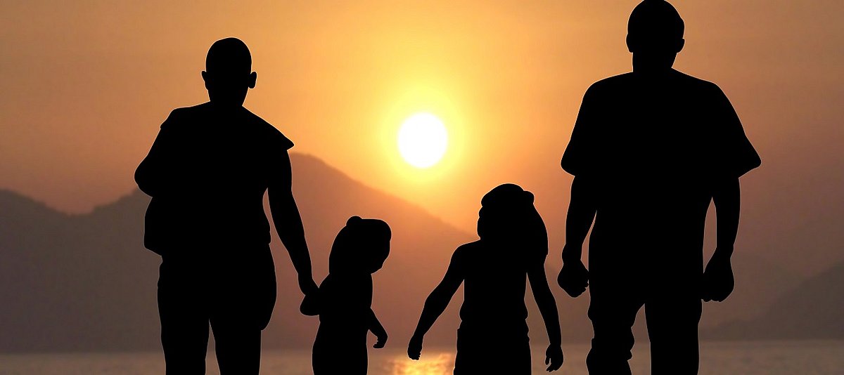 Eine vierköpfige Familie läuft durch die Wüste. Im Hintergrund geht die Sonne unter.