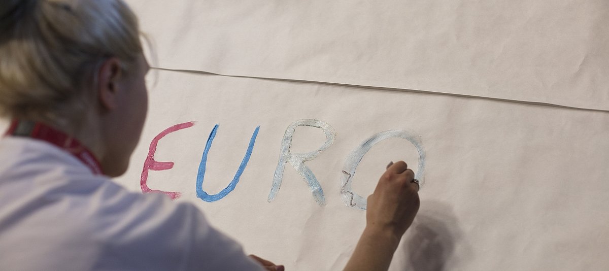 Ein junges Mädchen schreibt das Wort Europa mit bunten Buchstaben auf ein Plakat