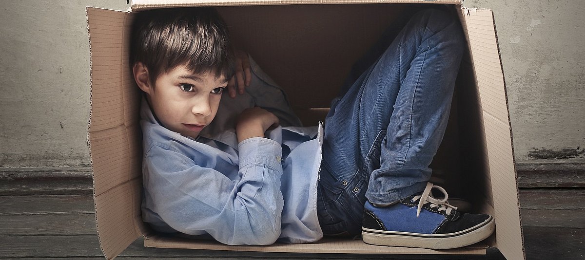 Ein Junge sitzt zusammengekauert in einem seitlich aufgestellten Karton