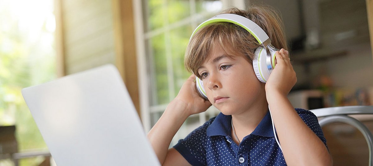 Ein Junge im Grundschulalter sitzt mit Kopfhörern vor einen Laptop.