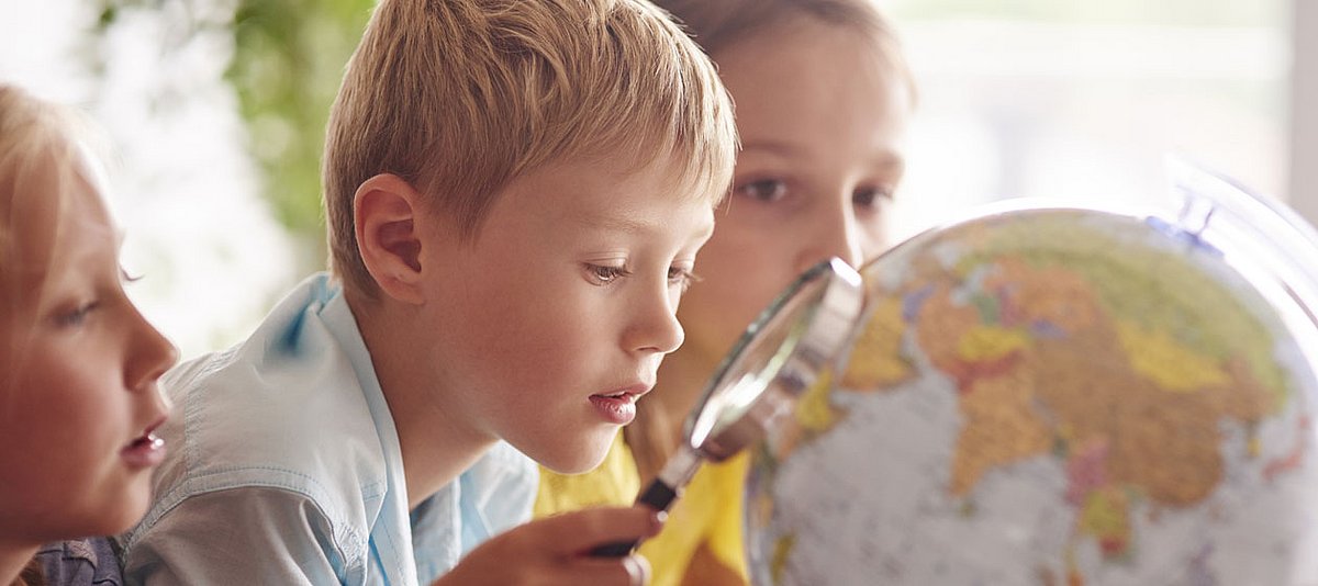 Drei Kinder im Grundschulalter schauen sich mit einer Lupe einen Globus an