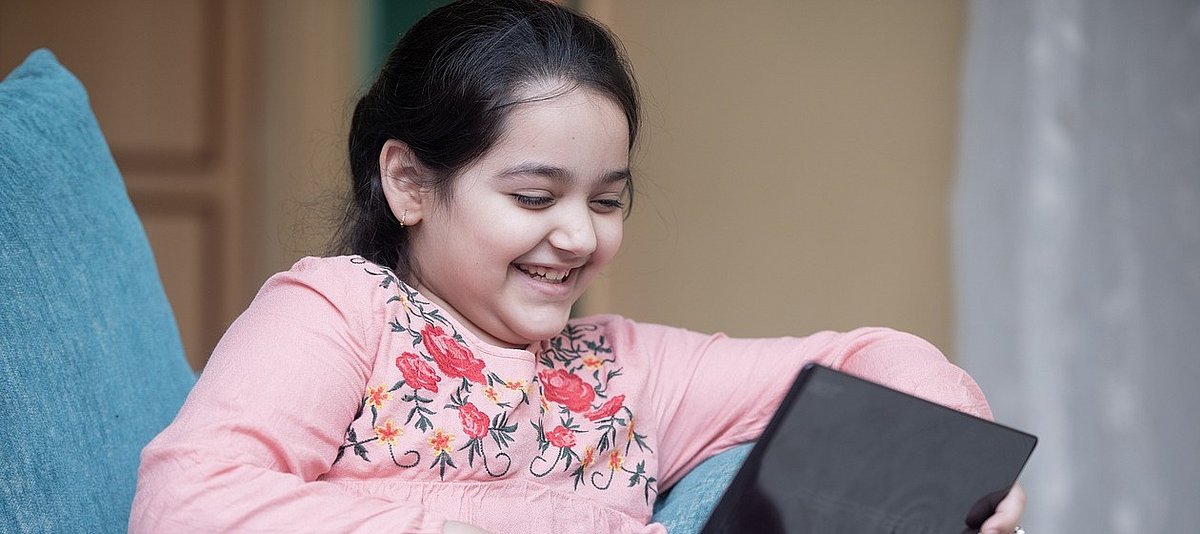 Ein Kind schaut auf einem Tablet einen Film an und lächelt