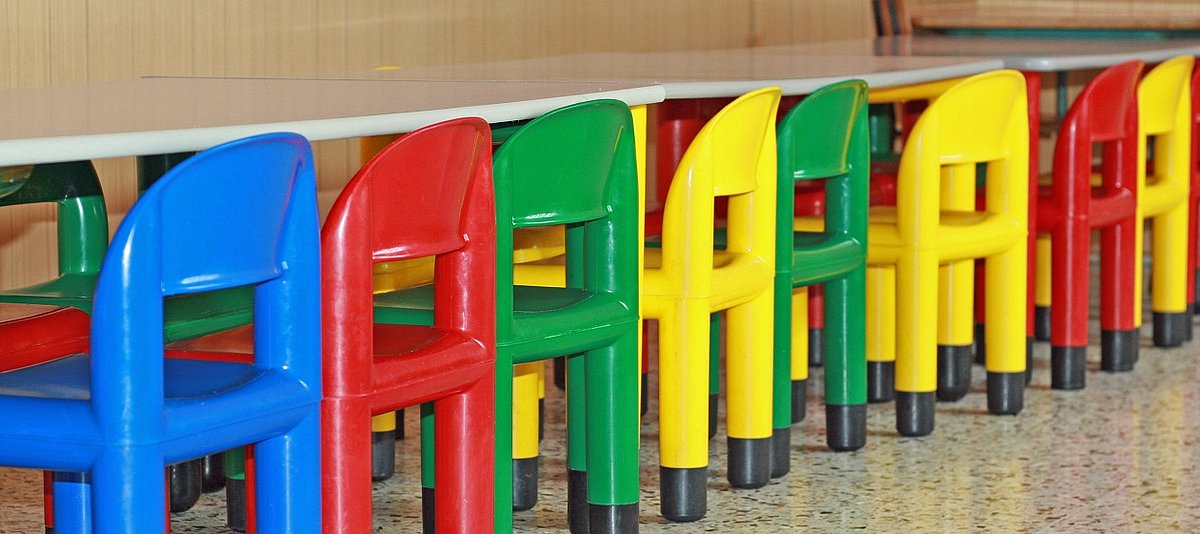 bunte Stühle für Kinder stehen an einem langen Tisch