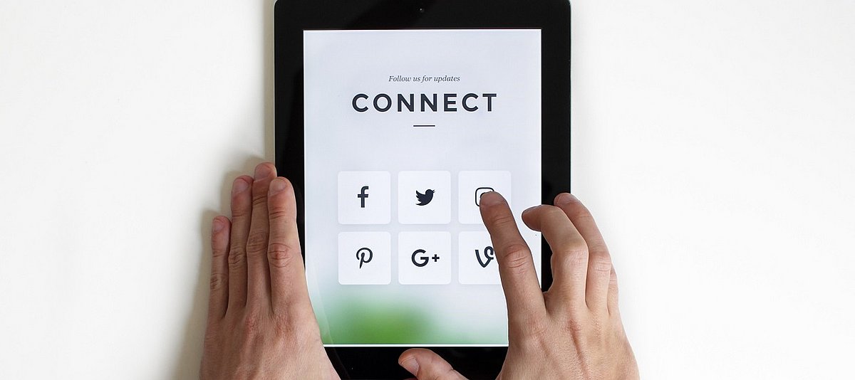 Zwei Hände bedienen ein Tablet auf dem Social Media Icons abgebildet sind