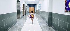 Ein Junge mit Schulranzen rennt durch einen leeren Flur eines Schulgebäudes