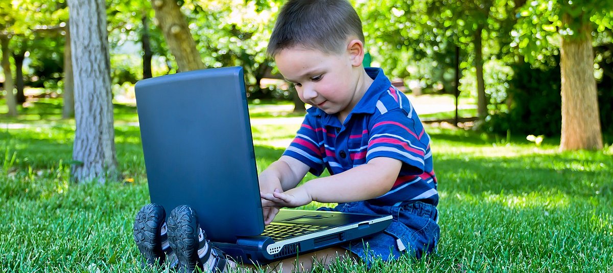 Ein kleiner Junge sitzt am Laptop und spielt damit.