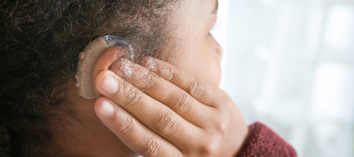 Ein Mädchen hält ihre Finger an ihrem Hörgerät am Ohr