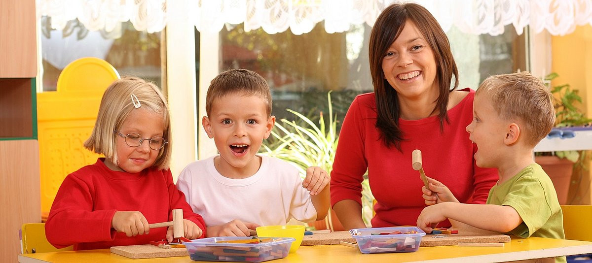 Zusammen mit der Betreuerin spielen drei Kinder am Tisch.