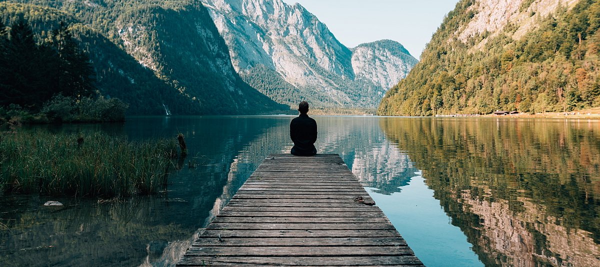 Eine Person sitzt alleine auf einem Steg und schaut auf einen Bergsee