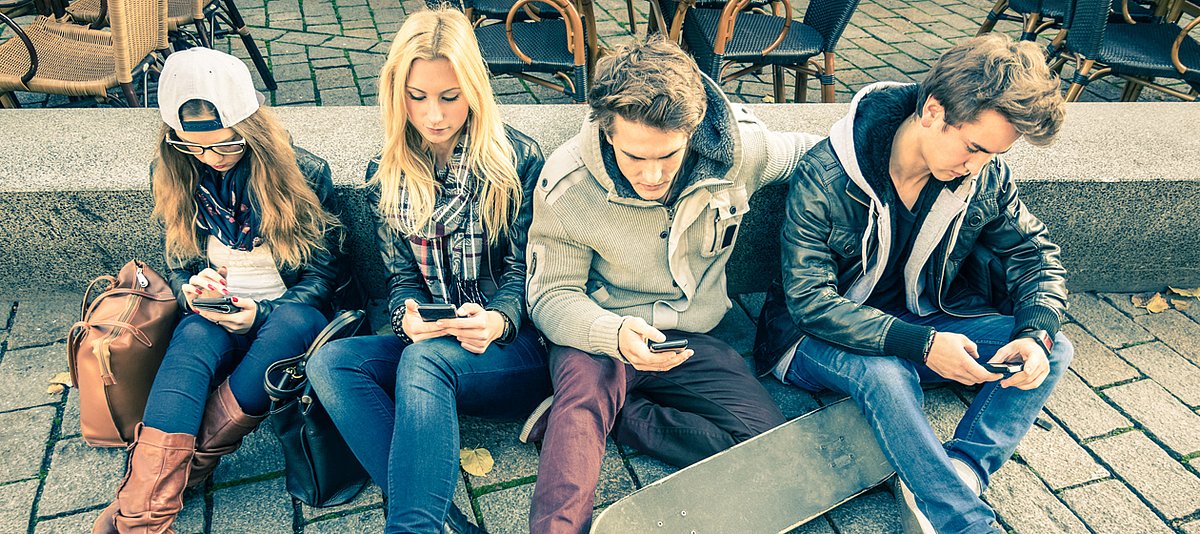 Jugendliche sitzen auf dem Boden mit Smartphone