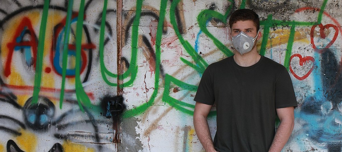 Jugendlicher mit Atemschutzmaske vor Wand mit Graffitis