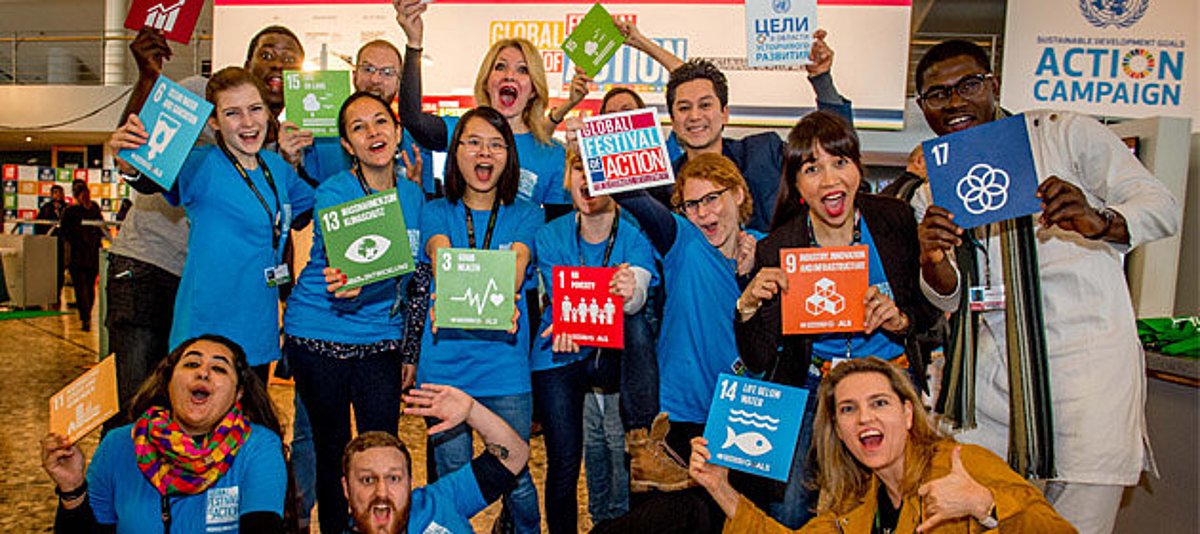 Gruppenfoto mit Teilnehmenden des UN-Festivals in blauen T-Shirts mit den SDG auf Postern in den Händen und lachen in die Kamera