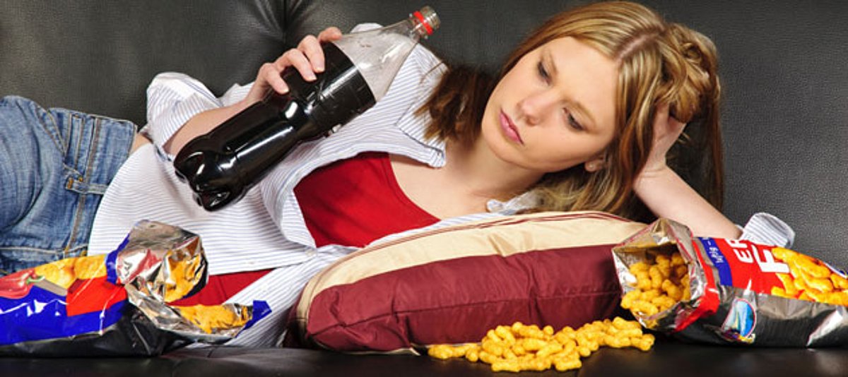 Ein Mädchen liegt auf dem Sofa und konsumiert Junkfood