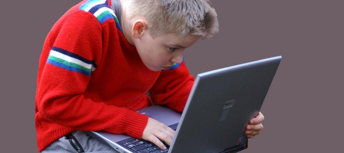 Junge sitzt verkrampft vor einem Laptop, den er auf seinem Schoß stehen hat