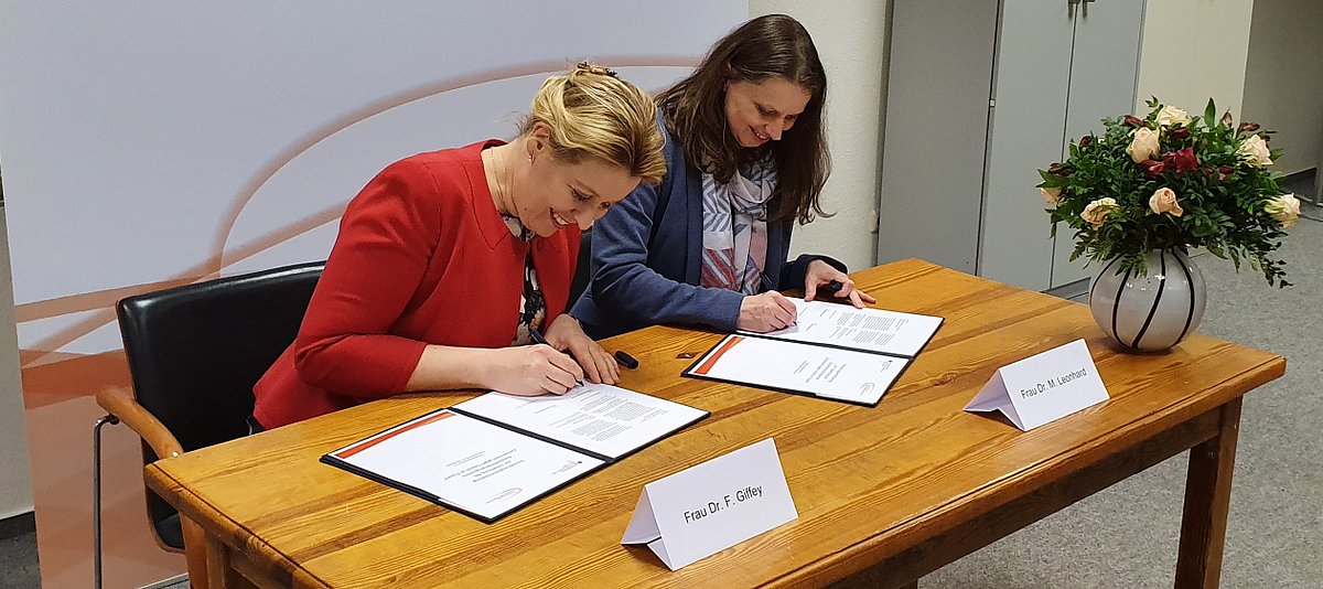 Bundesministerin Dr. Franziska Giffey und Senatorin Dr. Melanie Leonhard sitzen an einem Tisch und unterschreiben einen Vertrag
