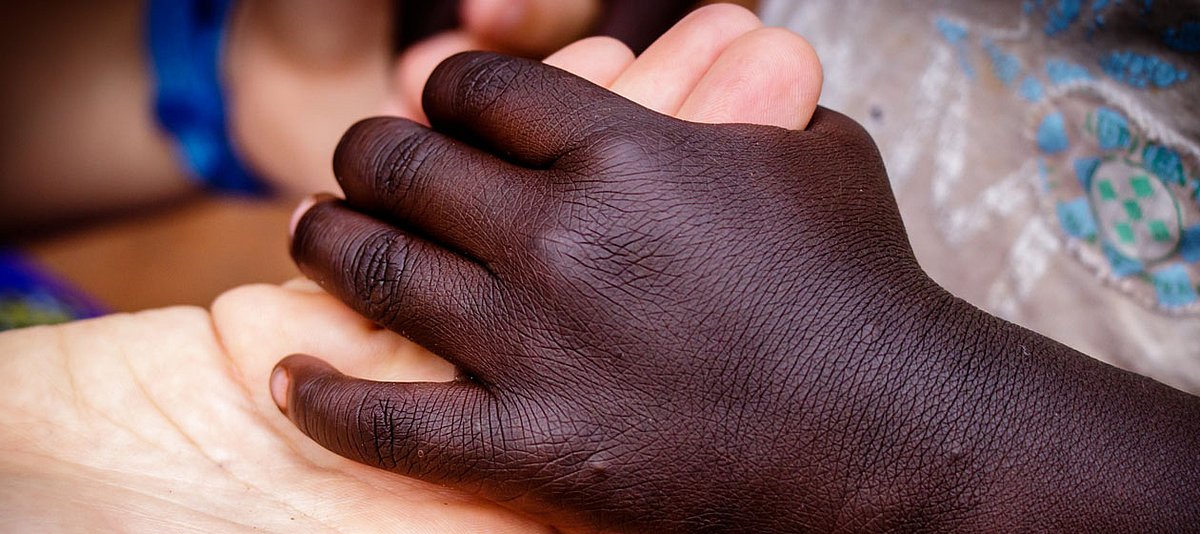 Zwei Hände von Menschen unterschiedlicher Herkunft liegen ineinander.