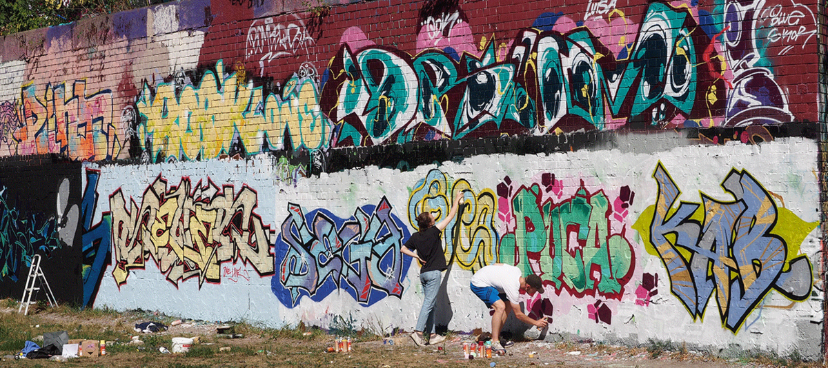 Zwei Jugendliche sprühen bunte Grafittis an einer Wand