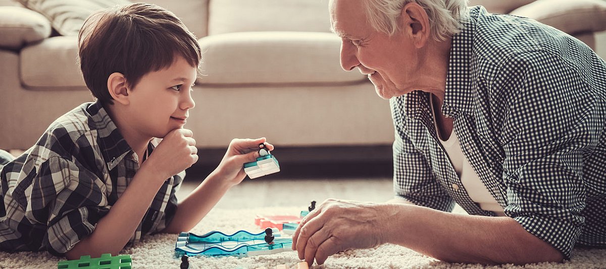 Ein Großvater spielt ein Gesellschaftsspiel mit seinem Enkel auf dem Wohnzimmerteppich.