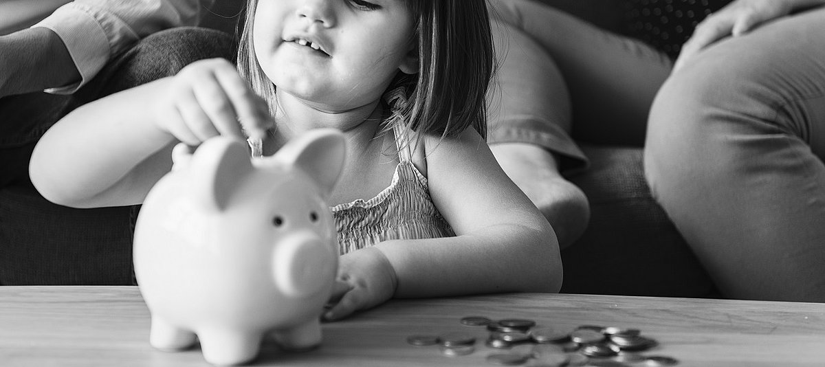 Ein Mädchen schmeißt Geld in ein Sparschwein