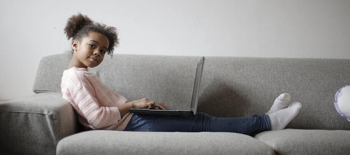 Auf dem Foto ist ein Mädchen zu sehen, das mit einem Laptop auf einer Couch sitzt.