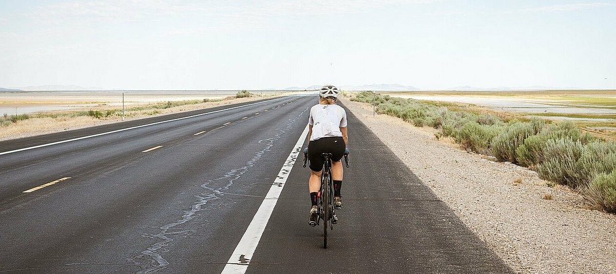 Frau in Sportbekleidung fährt Fahrrad auf einer breiten Straße durch ein Flachland