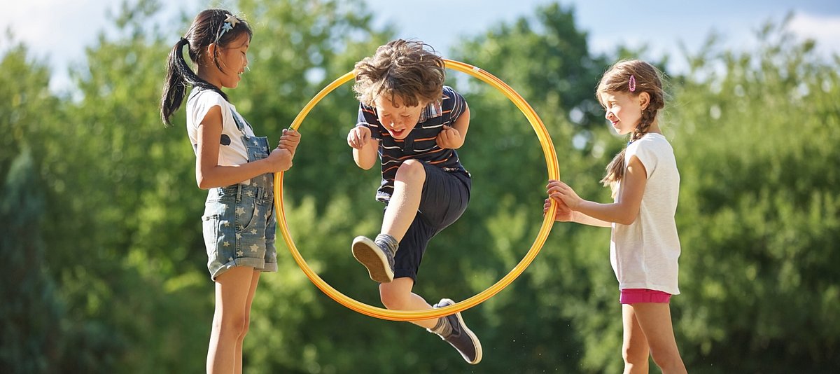 Junge springt durch Hula-Hoop-Reifen, der von zwei Mädchen gehalten wird